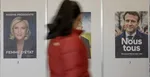 Volička kráča okolo predvolebných plagátov prezidentských kandidátov Marine Le Penovej a Emmanuela Macrona.